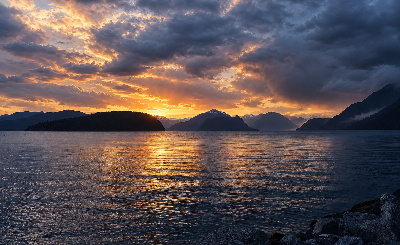 Howe Sound water and layered Coast Mountains along the Sea-to-Sky corridor beneath a dramatic sky